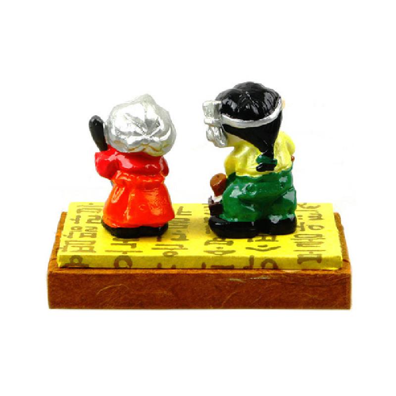 형형색색 채색된 한복 차림 남매 인형과 한글 패턴이 인쇄된 직사각형 받침대로 구성된 민속 장식품.