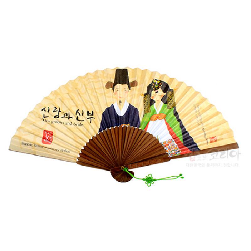 한지 재질 위에 전통 혼례복을 입은 신랑·신부 일러스트가 그려진 접선, 나뭇결 살대와 녹색 매듭 장식이 어우러진 부채. 한지 재질 위에 전통 혼례복을 입은 신랑·신부 일러스트가 그려진 접선, 나뭇결 살대와 녹색 매듭 장식이 어우러진 부채.