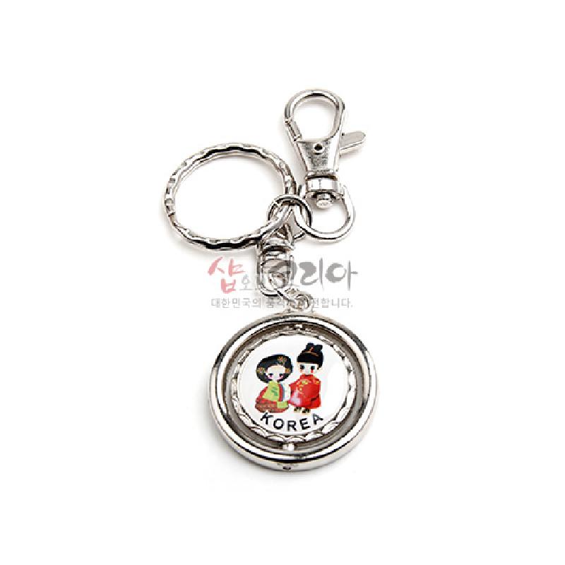 은색 금속 원형 테두리에 한복 입은 남녀 일러스트와 KOREA 문구가 들어간 컬러 인쇄 장식 열쇠고리.