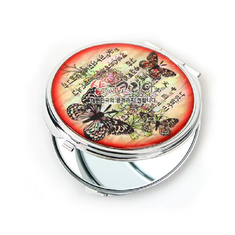 자개 장식 금속 손거울, 붉은 그러데이션 배경 위에 나비와 꽃, 훈민정음 서체 문양이 어우러진 디자인. 자개 장식 금속 손거울, 붉은 그러데이션 배경 위에 나비와 꽃, 훈민정음 서체 문양이 어우러진 디자인.