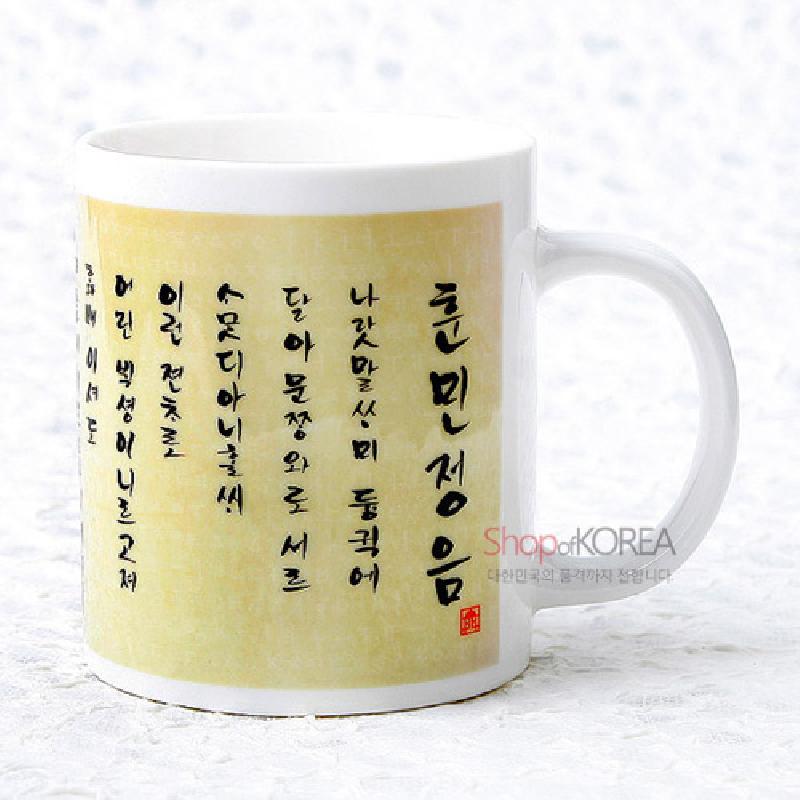 흰색 도자기로 제작된 머그컵에 옅은 노랑 배경과 훈민정음 서예체 글씨가 연속 배치된 디자인.