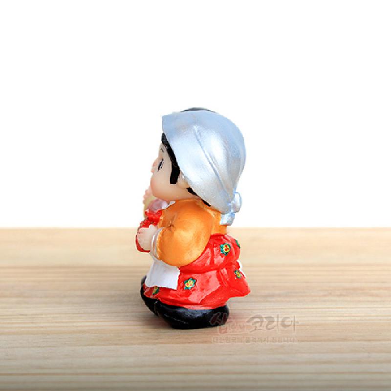 은색 머릿수건과 주황 저고리, 붉은 치마에 꽃무늬를 그려 넣은 복주머니 든 소형 민속 인형. 은색 머릿수건과 주황 저고리, 붉은 치마에 꽃무늬를 그려 넣은 복주머니 든 소형 민속 인형.