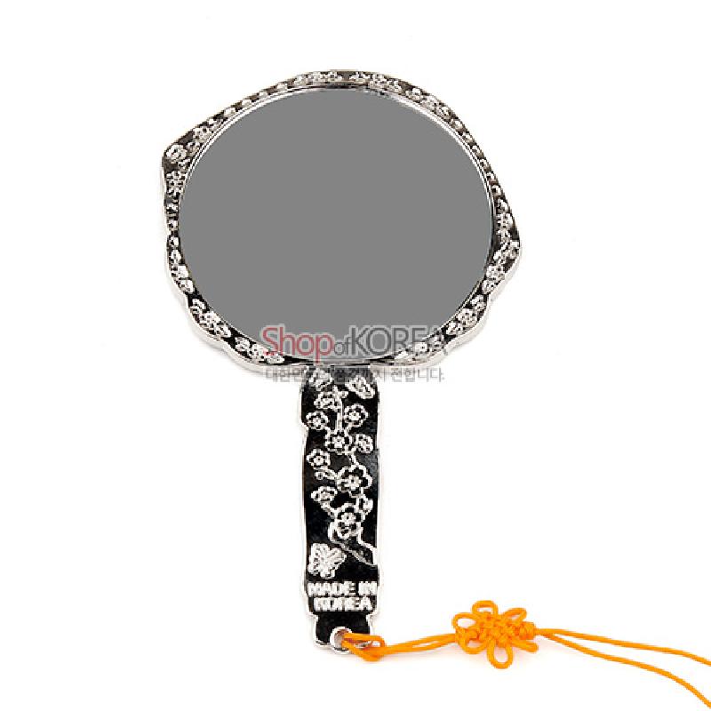 검은 바탕 금속 위에 흰색 꽃무늬가 상감된 원형 손잡이 거울, 오렌지색 매듭 장식 끈이 달린 디자인.