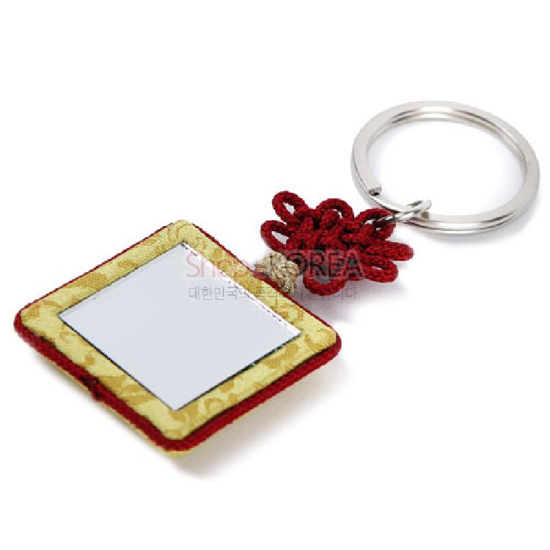 황색 비단 조각보 테두리와 사각 거울 장식, 붉은 전통 매듭과 금속 링이 연결된 열쇠고리형 장식.