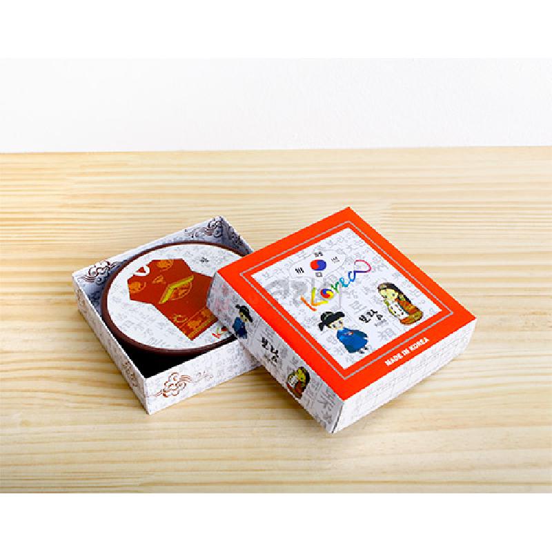 한복 모양 문양이 인쇄된 빨간색 원형 컵받침과 한글·캐릭터 일러스트가 있는 종이 포장 상자 구성.