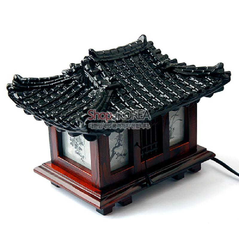 검은 기와 지붕과 붉은 목재 구조로 구현된 한옥 형태 스탠드, 창호지 부분의 수묵화 산수문 양각이 돋보이는 조명 장식. 검은 기와 지붕과 붉은 목재 구조로 구현된 한옥 형태 스탠드, 창호지 부분의 수묵화 산수문 양각이 돋보이는 조명 장식.