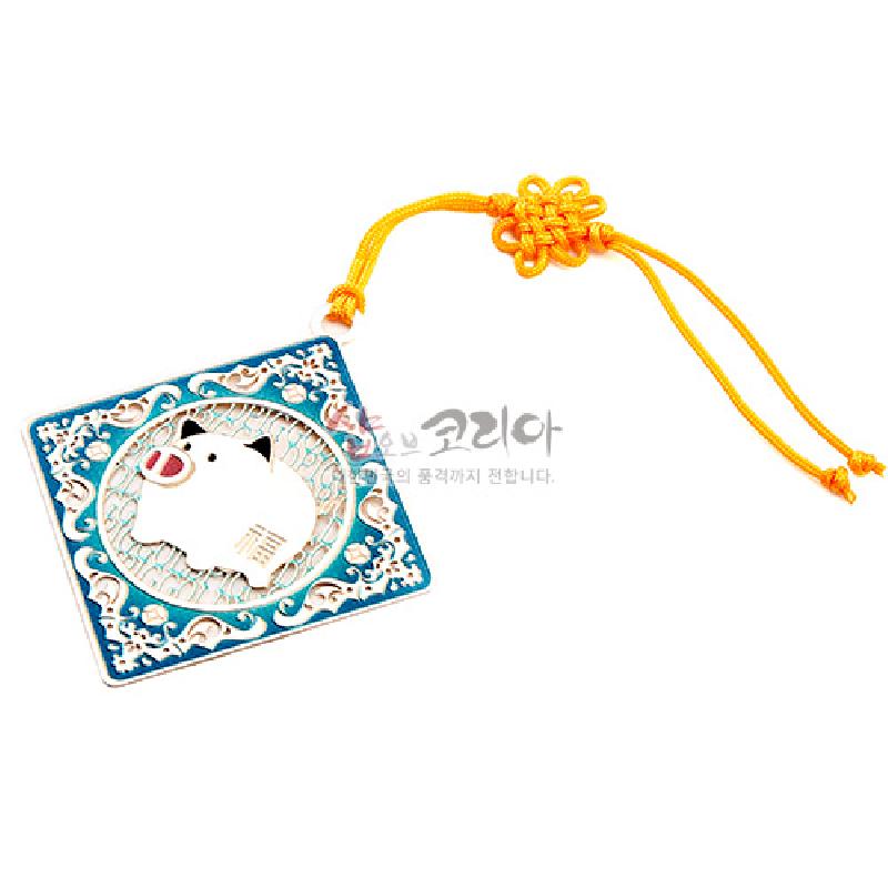 금속 재질의 사각 틀에 돼지와 구름 문양을 상감한 책갈피, 청록색 바탕과 노란 전통 매듭 끈 장식.