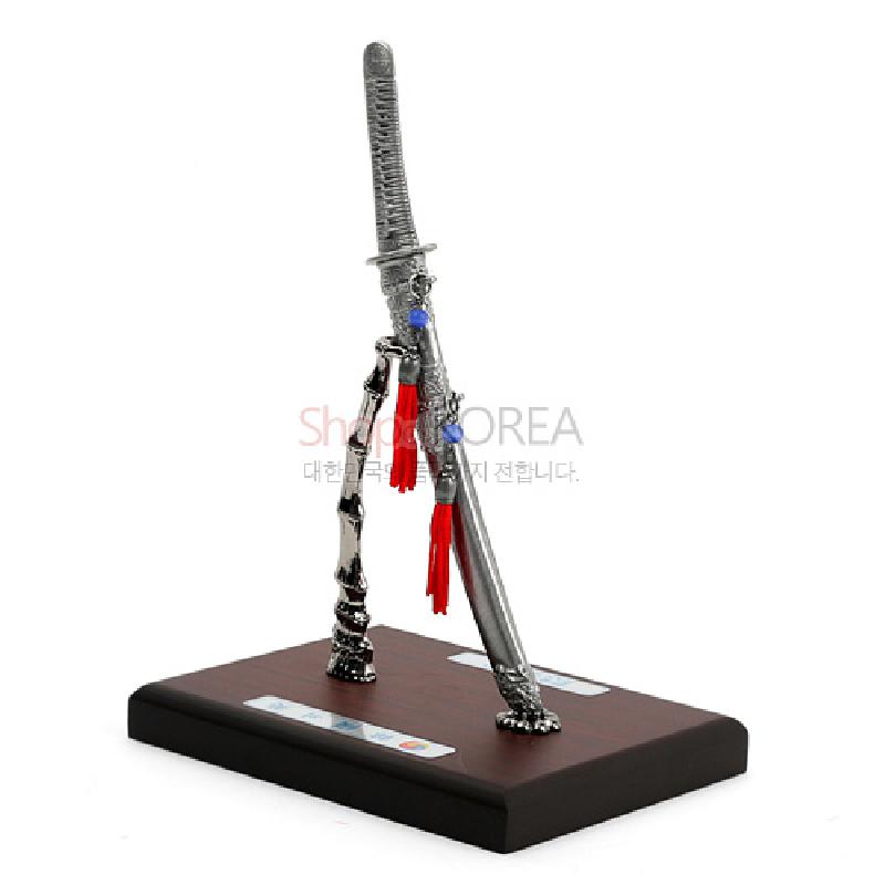 금속 재질의 한국도와 칼집을 세로로 세운 스탠드형 장식, 붉은 술과 청색 구슬 장식이 포인트인 금속 공예품.