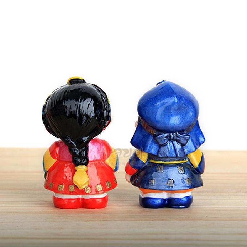 붉은색과 파란색 한복 차림의 남녀를 형상화한 소형 민속 인형, 유광 채색과 금색 장식이 돋보이는 도자 장식품. 붉은색과 파란색 한복 차림의 남녀를 형상화한 소형 민속 인형, 유광 채색과 금색 장식이 돋보이는 도자 장식품.