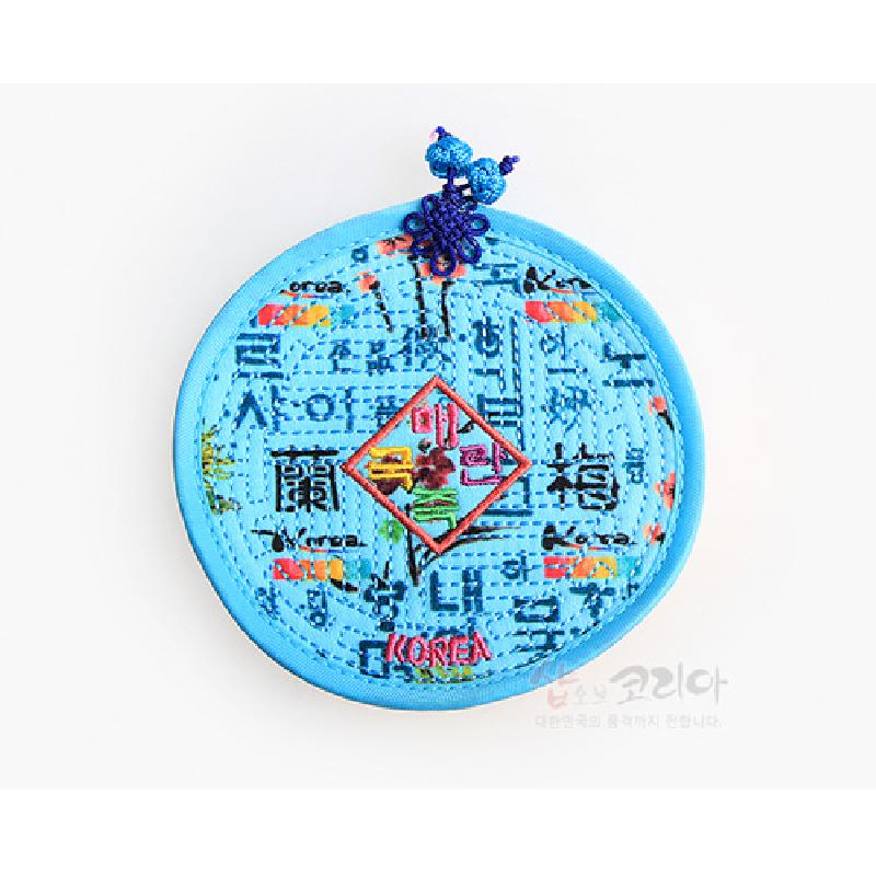 밝은 하늘색 천 누비 기법에 훈민정음 문자 패턴과 다채로운 수놓기, 장식 매듭 고리가 더해진 원형 컵받침.