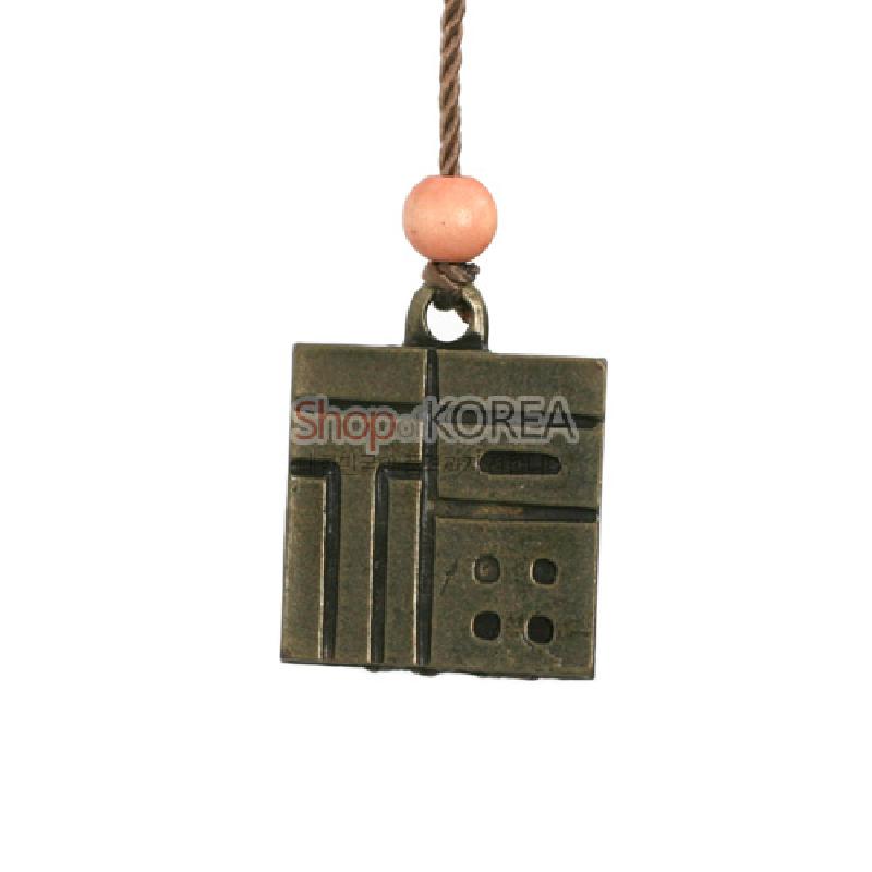 앙금색 금속 재질의 사각형 장식으로, 기하학적 선각과 구멍 문양, 윗부분 나무 구슬 매듭이 특징인 복주머니 장식.