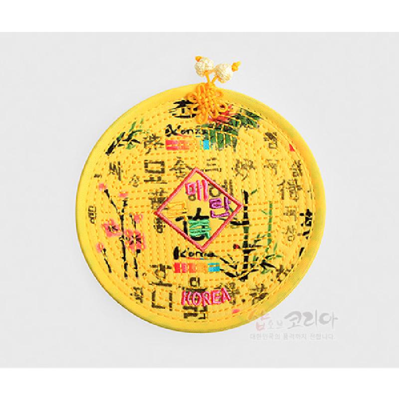 노란 색상의 누비 천 위에 훈민정음 글자와 대나무, 매화 자수 문양이 어우러진 원형 컵받침.