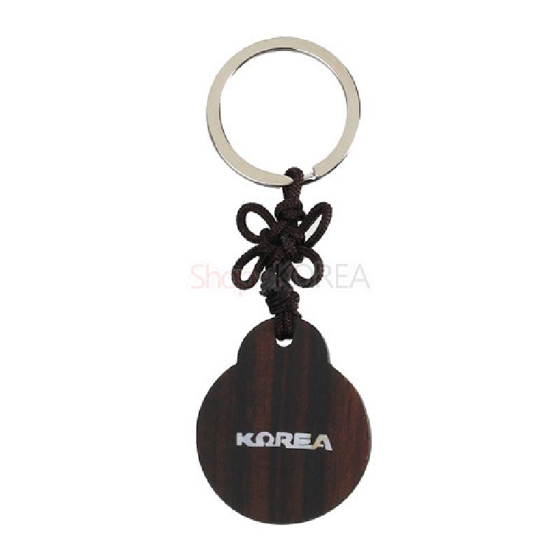 흑단 소재의 원형 장식에 매듭기법을 사용한 끈을 연결하고, 앞면에 흰색 ‘KOREA’ 문양이 인쇄된 열쇠고리