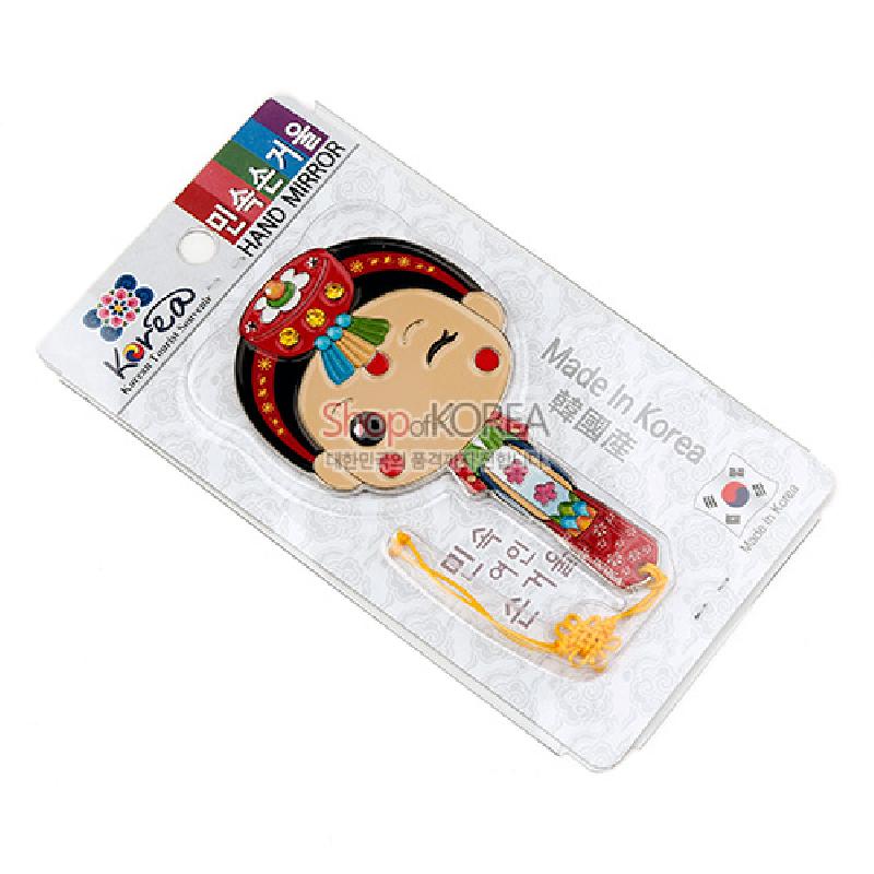 금속 재질 위에 한복 신부 얼굴을 형상화한 손거울, 붉은색과 초록색 전통 문양과 노란 매듭 장식이 있는 디자인.