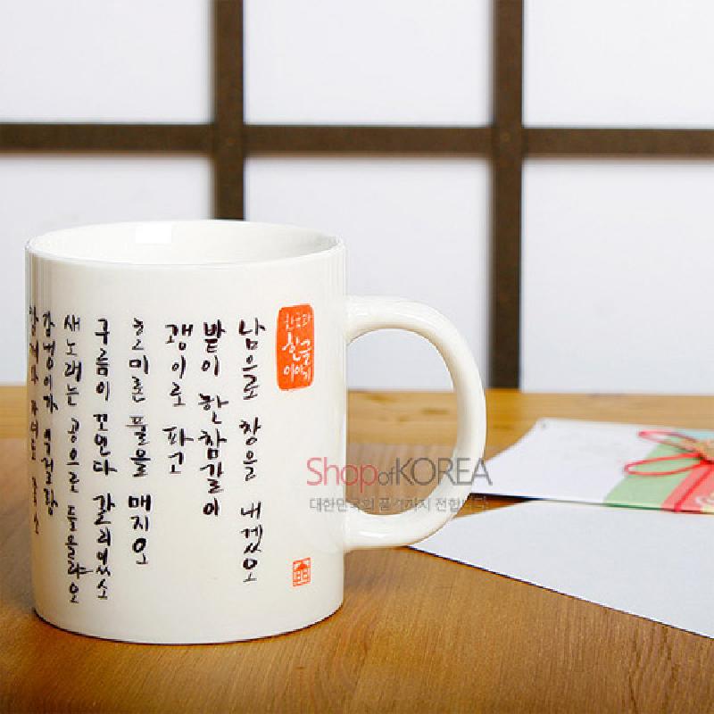 백색 도자 재질에 검은색 세로 한글 시와 붉은 전각 문양이 어우러진 머그컵.