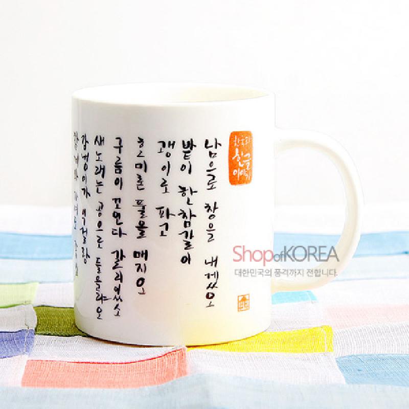 백자 느낌의 흰 도자기 재질에 검은색 손글씨 한글 서체와 붉은 전각 인장이 장식된 머그컵.
