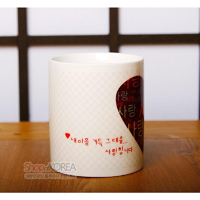 하트 모양 절개 안쪽에 빨강·검정 배경과 한글 사랑 문양을 넣은 흰색 도자기 머그컵.