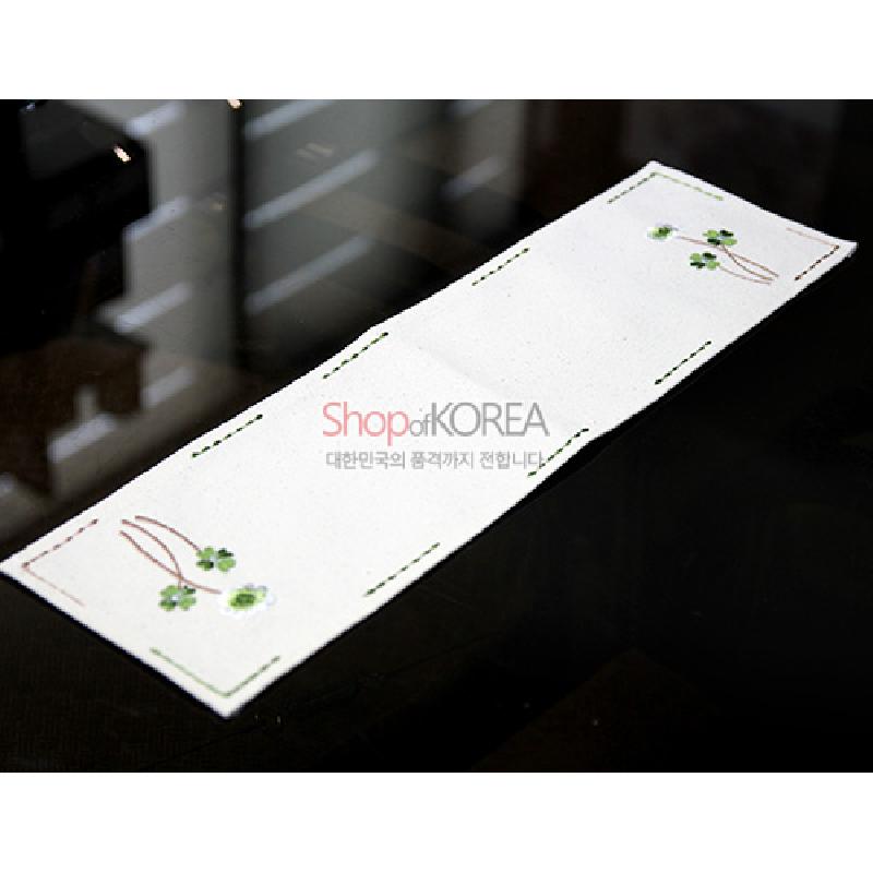 광목 소재에 초록 네잎클로버와 흰꽃 자수 문양, 가장자리 선형 스티치 장식이 더해진 흰색 식탁보.