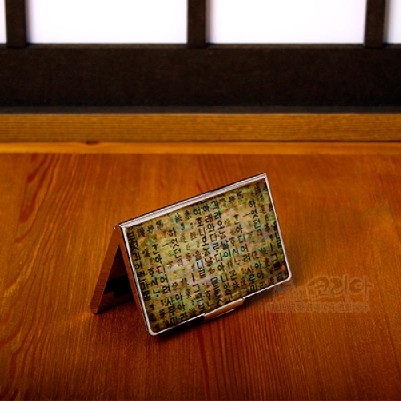 금속 테두리에 한지 배경과 훈민정음 글자 문양을 더한 갈색 톤의 직사각형 명함케이스. 금속 테두리에 한지 배경과 훈민정음 글자 문양을 더한 갈색 톤의 직사각형 명함케이스.