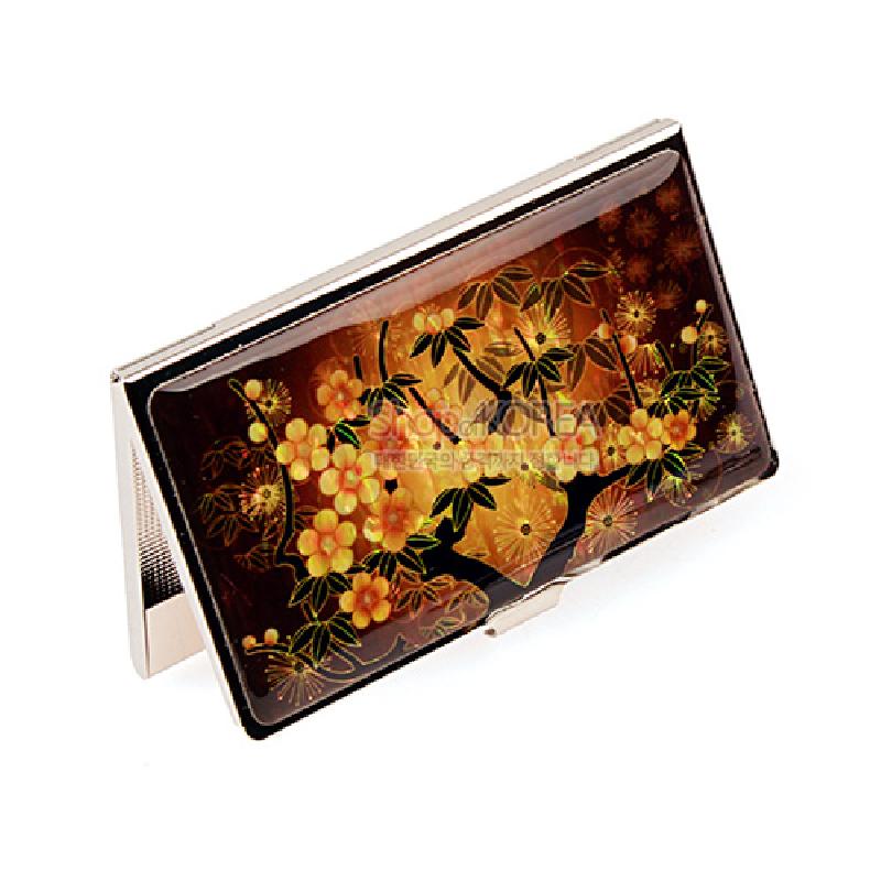 황색과 갈색 배경 위 자개 느낌의 매화꽃과 가지 문양이 장식된 금속 명함케이스.