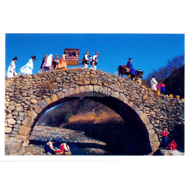전통 혼례 행렬과 돌다리 풍경을 담은 사진 엽서, 푸른 하늘과 자연색이 조화를 이룬 디자인.