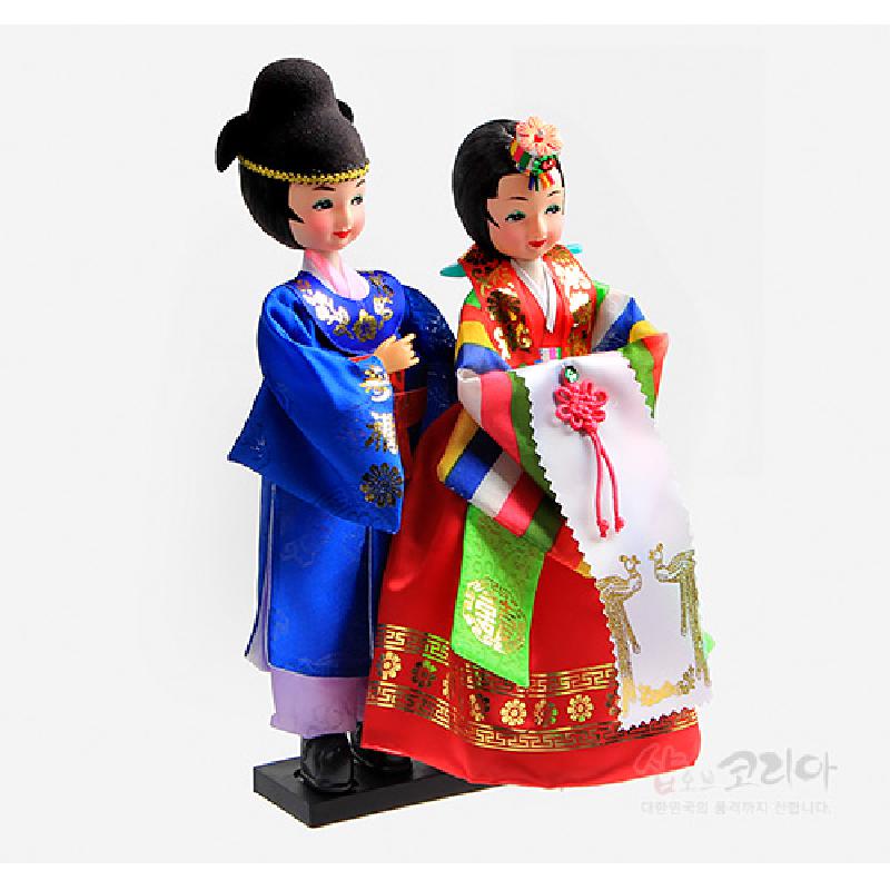 비단 재질의 한복을 입은 신랑신부 인형으로, 청색과 홍색 대비 색상과 금박 전통 문양, 오방색 소매와 매듭 장식이 특징인 장식 인형.