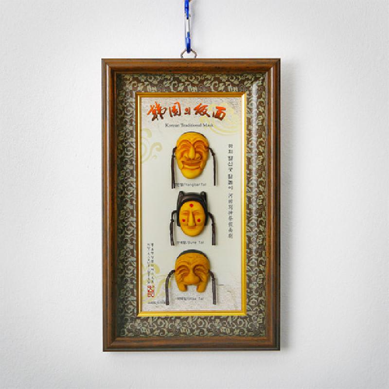 나무 재질 액자에 황토색 하회탈 3형 미니어처를 세로 배열한 구성과 전통 문양 장식 배경이 돋보이는 인테리어 액자. 나무 재질 액자에 황토색 하회탈 3형 미니어처를 세로 배열한 구성과 전통 문양 장식 배경이 돋보이는 인테리어 액자.