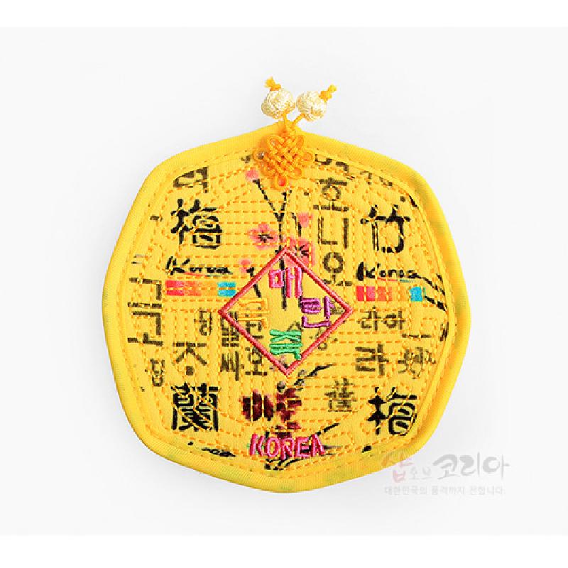 노란색 천에 누비 기법으로 제작된 팔각 컵받침, 훈민정음 문자와 매화 자수, 전통 매듭 장식이 돋보이는 디자인. 노란색 천에 누비 기법으로 제작된 팔각 컵받침, 훈민정음 문자와 매화 자수, 전통 매듭 장식이 돋보이는 디자인.