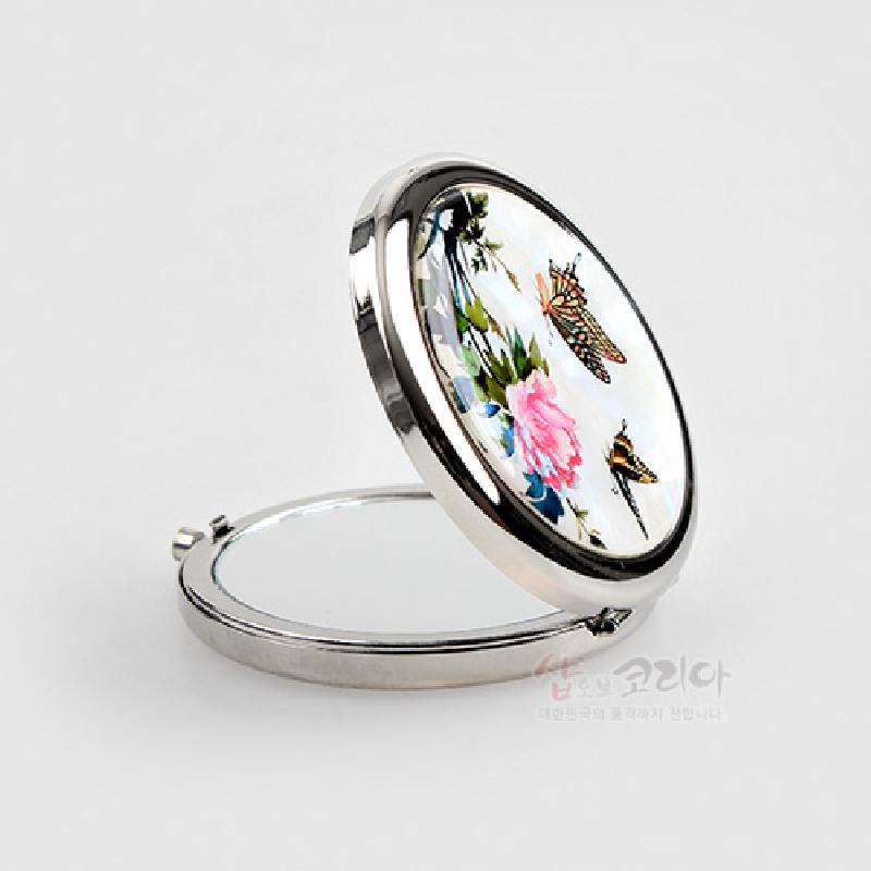 자개로 장식된 금속 원형 손거울, 흰 바탕 위에 담홍색 꽃과 나비 문양이 어우러진 디자인.