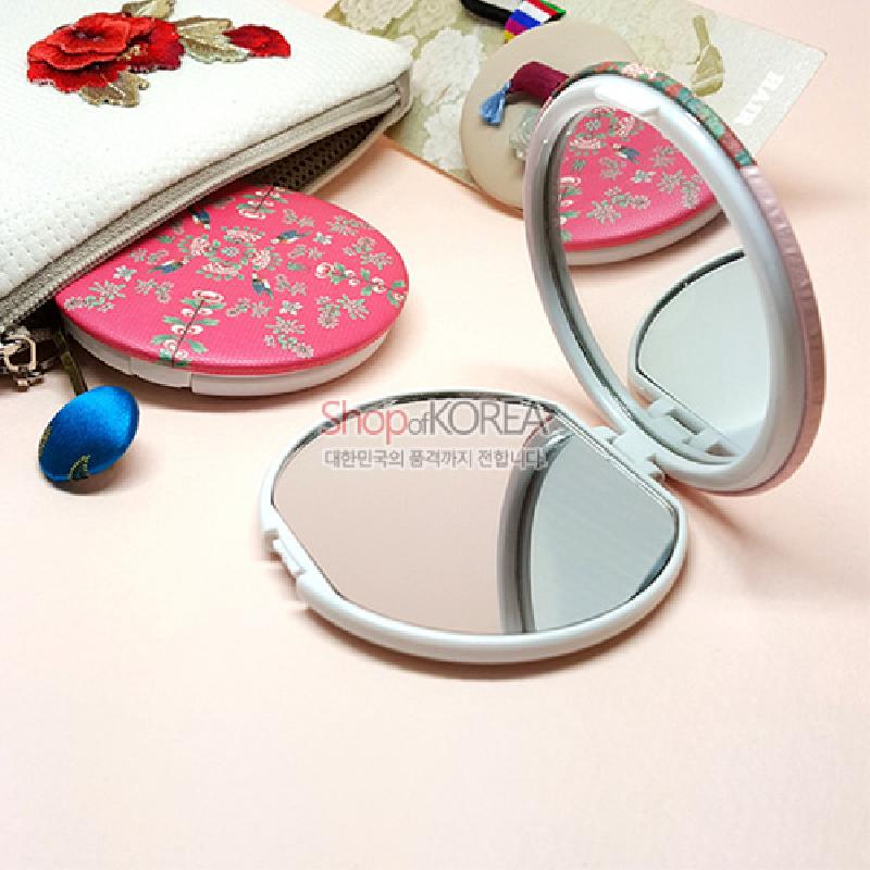 분홍색 바탕 위에 은빛 꽃무늬가 인쇄된 플라스틱 양면 손거울, 가장자리에 조각보 패턴 장식이 들어간 디자인.