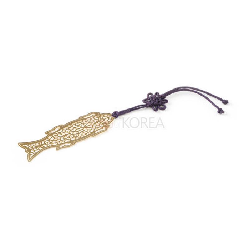 금장 금속으로 제작된 물고기 모양의 투각 문양 책갈피와 보라색 전통 매듭 장식 끈 구성. 금장 금속으로 제작된 물고기 모양의 투각 문양 책갈피와 보라색 전통 매듭 장식 끈 구성.