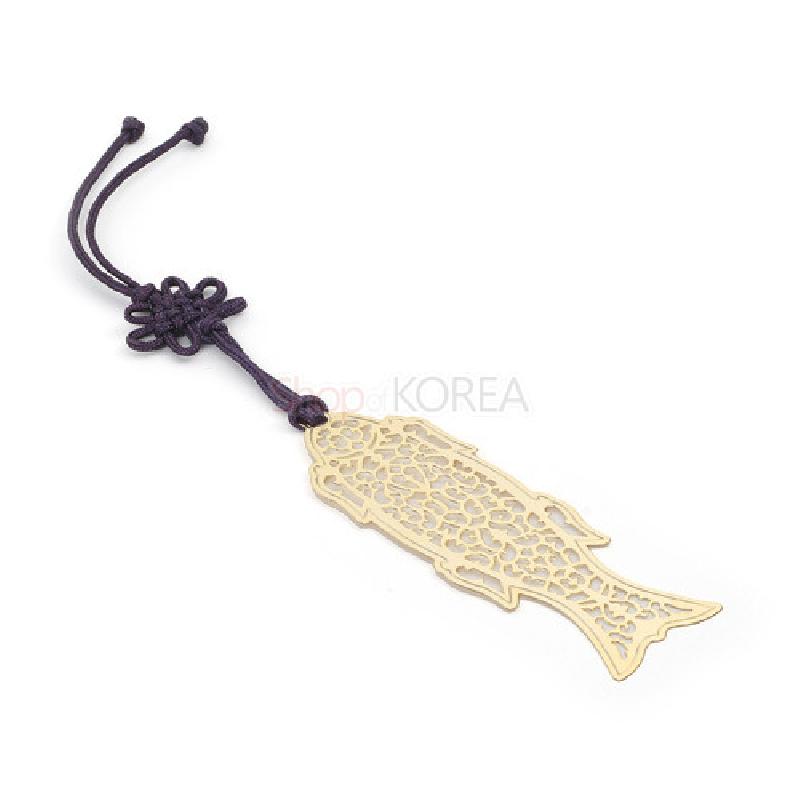금색 금속 재질에 물고기 형태를 섬세한 투각 기법으로 표현하고, 진한 보라색 전통 매듭 장식 끈이 연결된 책갈피. 금색 금속 재질에 물고기 형태를 섬세한 투각 기법으로 표현하고, 진한 보라색 전통 매듭 장식 끈이 연결된 책갈피.