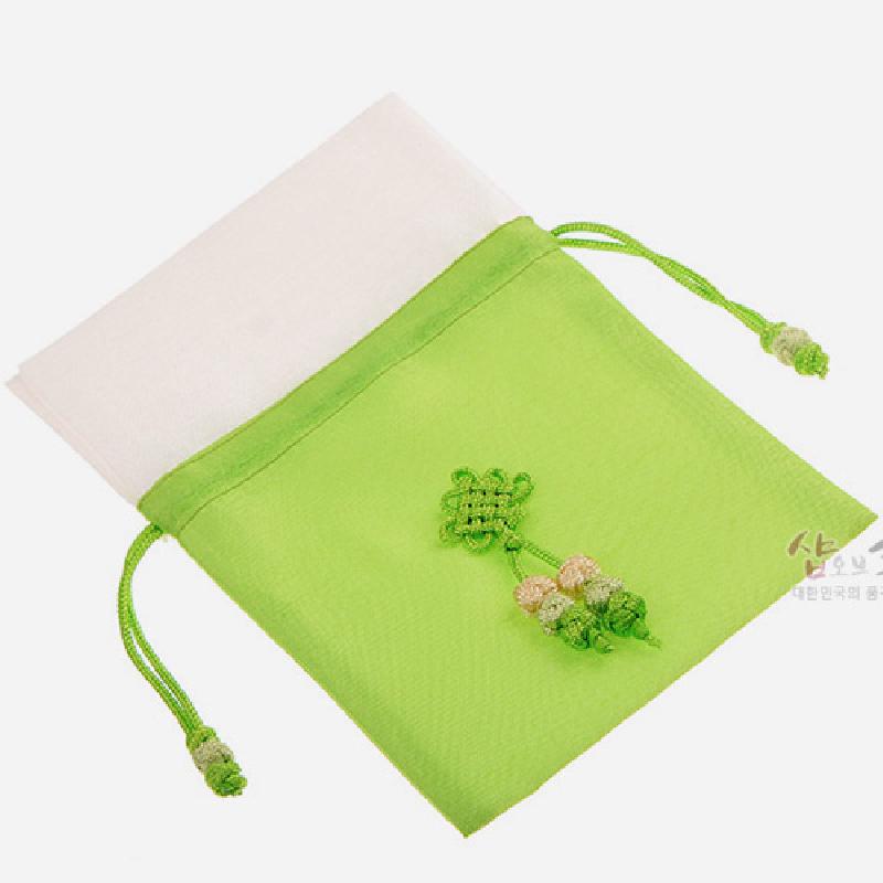 연두색과 흰색 배색의 비단 소재, 중앙에 전통 매듭과 술 장식이 더해진 끈 조절 주머니.