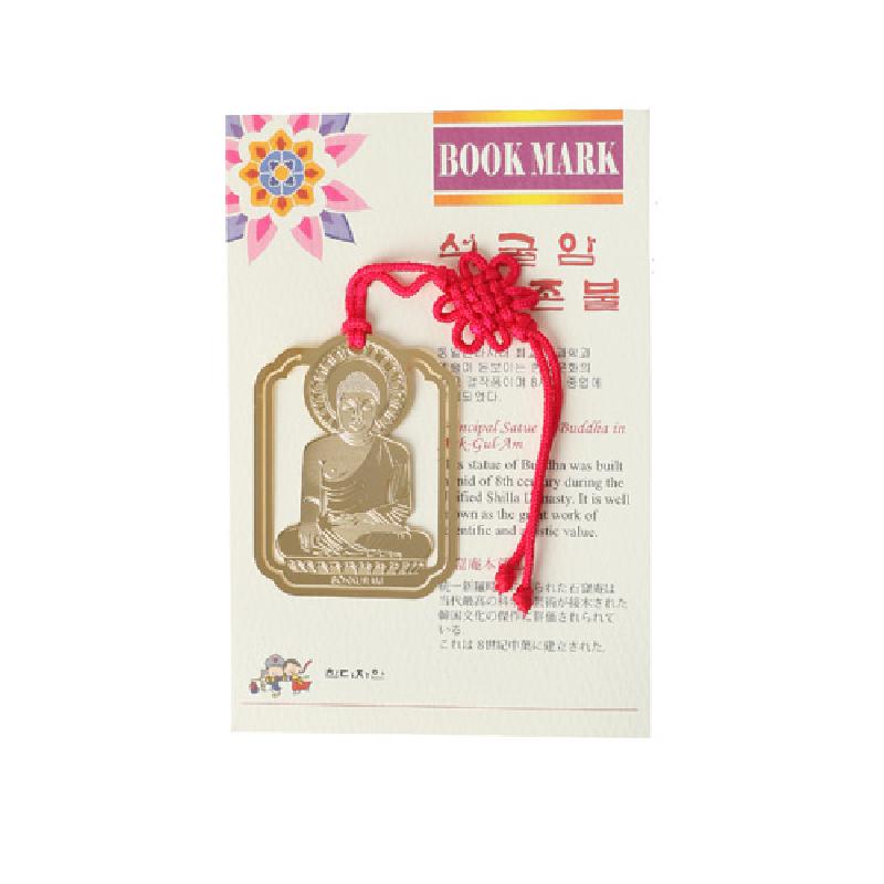 금속 재질에 석굴암 본존불을 정교하게 음각한 금장 책갈피와 붉은 전통 매듭 장식 끈이 어우러진 디자인. 금속 재질에 석굴암 본존불을 정교하게 음각한 금장 책갈피와 붉은 전통 매듭 장식 끈이 어우러진 디자인.