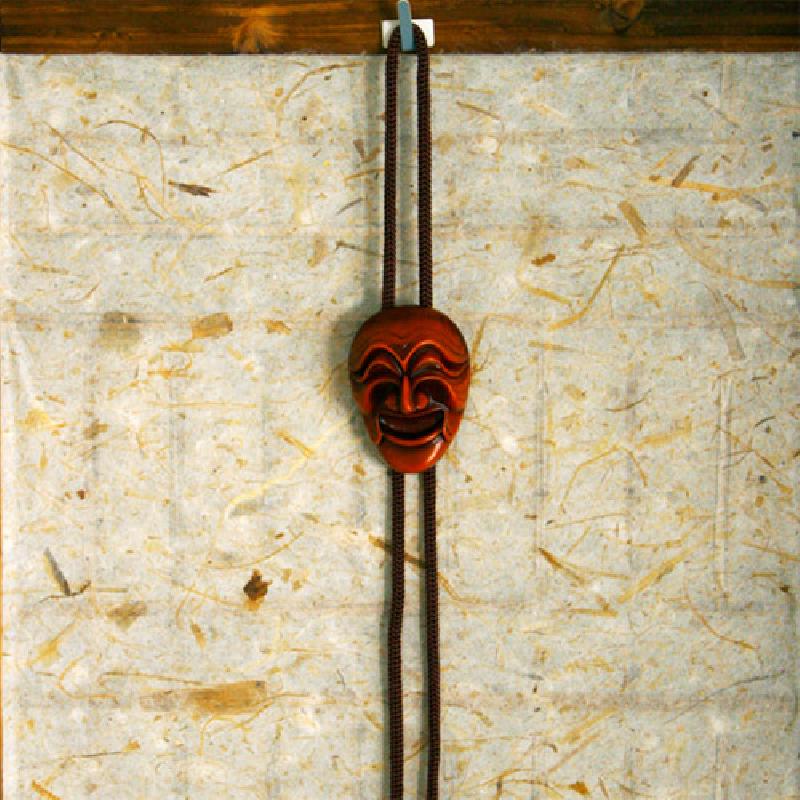 갈색 목재 재질의 양반탈 장식과 어두운 색 직조 로프가 조화를 이룬 로프타이.