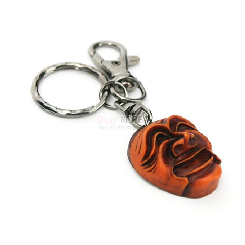 주황빛과 갈색이 어우러진 양반탈 형태의 조각 장식, 은색 금속 고리와 연결된 열쇠고리.