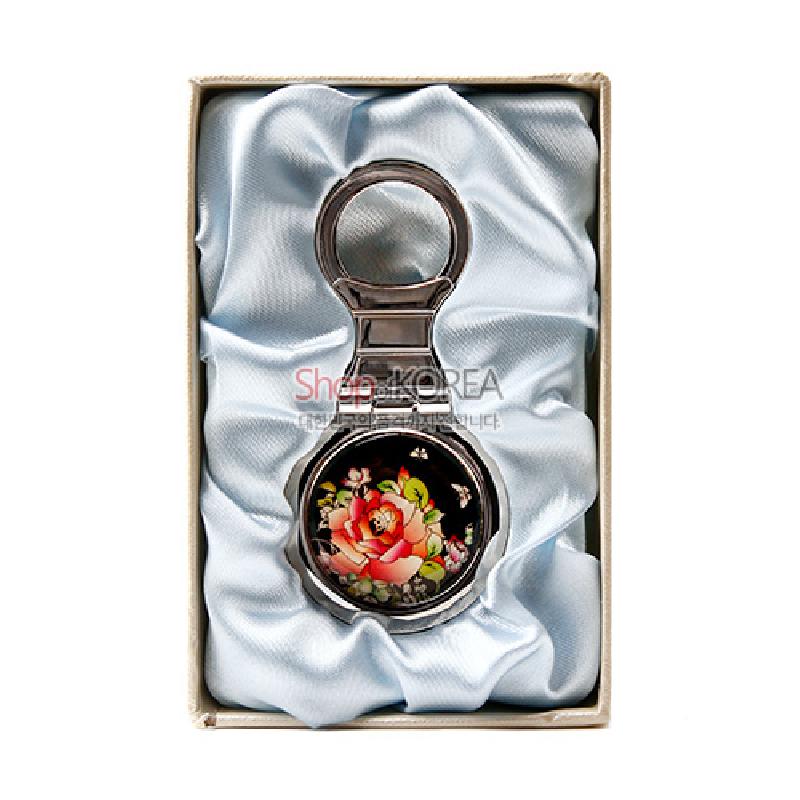 검은 바탕 위 자개 상감으로 장미와 꽃무늬를 표현한 원형 금속 열쇠고리 장식.