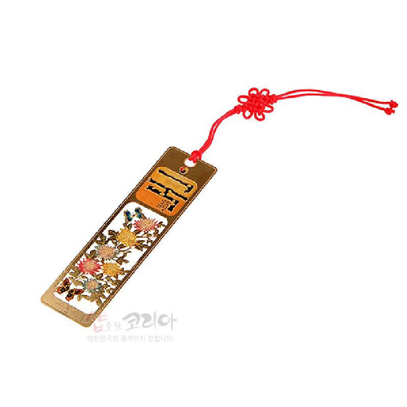 금속 재질에 금장 처리된 직사각형 책갈피, 국화 문양 투각 장식과 붉은 실 매듭 장식이 돋보이는 디자인.
