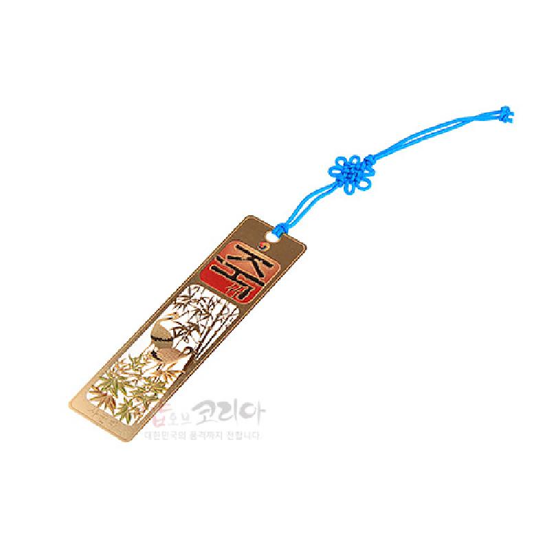 금속 재질에 금장 처리된 직사각형 책갈피, 대나무와 새 문양의 투각 기법과 붉은 한자 장식, 파란 색 끈 매듭 장식.