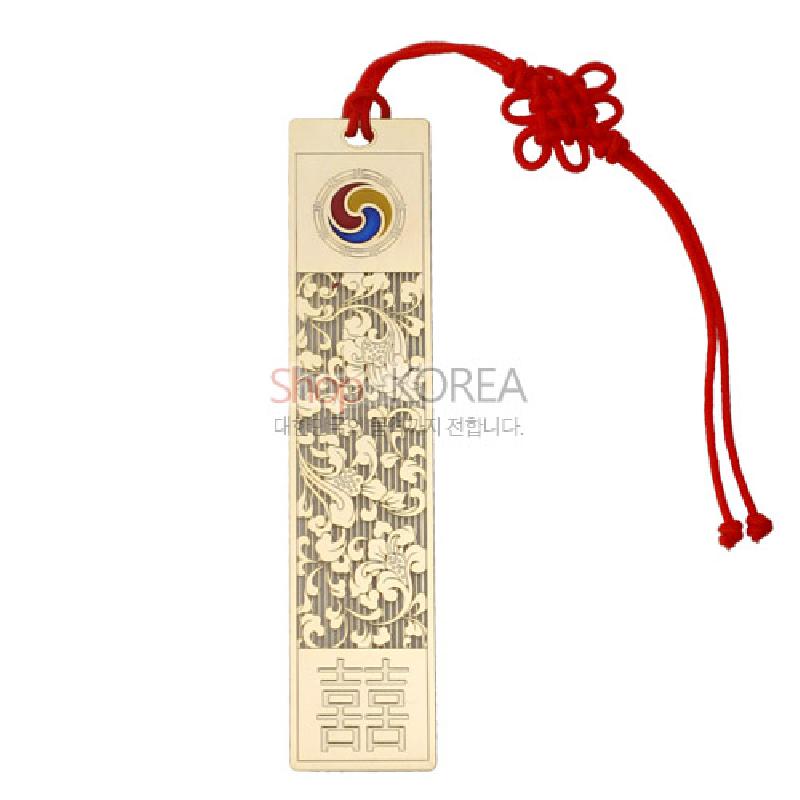 금속 재질에 금장 처리된 직사각형 책갈피, 당초문 양각 장식과 삼태극 문양, 붉은 전통 매듭 장식이 특징인 디자인.