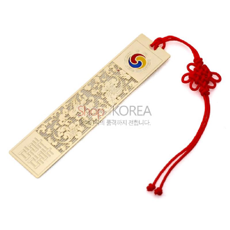 금장 금속 소재에 섬세한 당초문과 길상문양을 투각한 책갈피, 태극 문양 포인트와 붉은 전통 매듭 장식이 돋보이는 디자인.