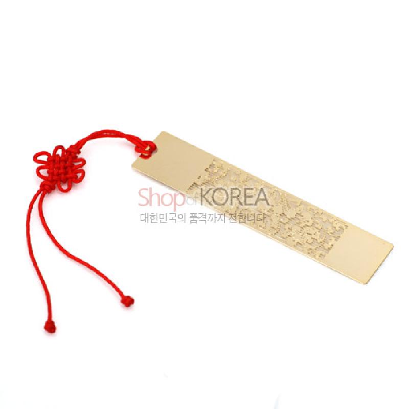 금속 소재에 당초문 양각 장식이 더해진 금장 책갈피와 붉은 전통 매듭 끈 장식.