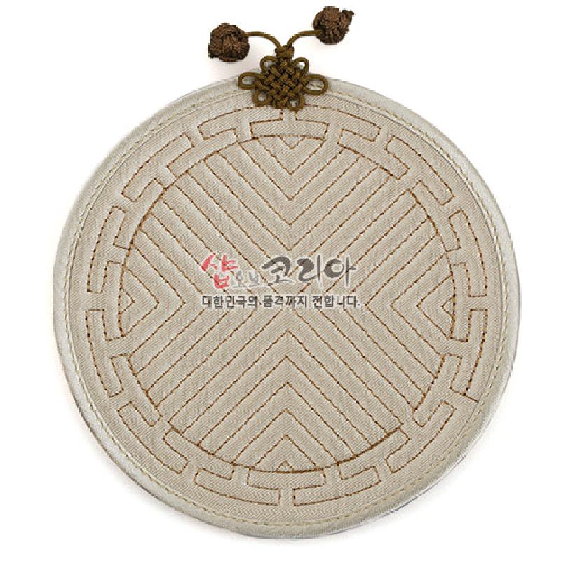 아이보리색 천에 누비 기법으로 기하학 문양을 넣고 윗부분에 갈색 전통 매듭 장식을 더한 원형 컵받침.