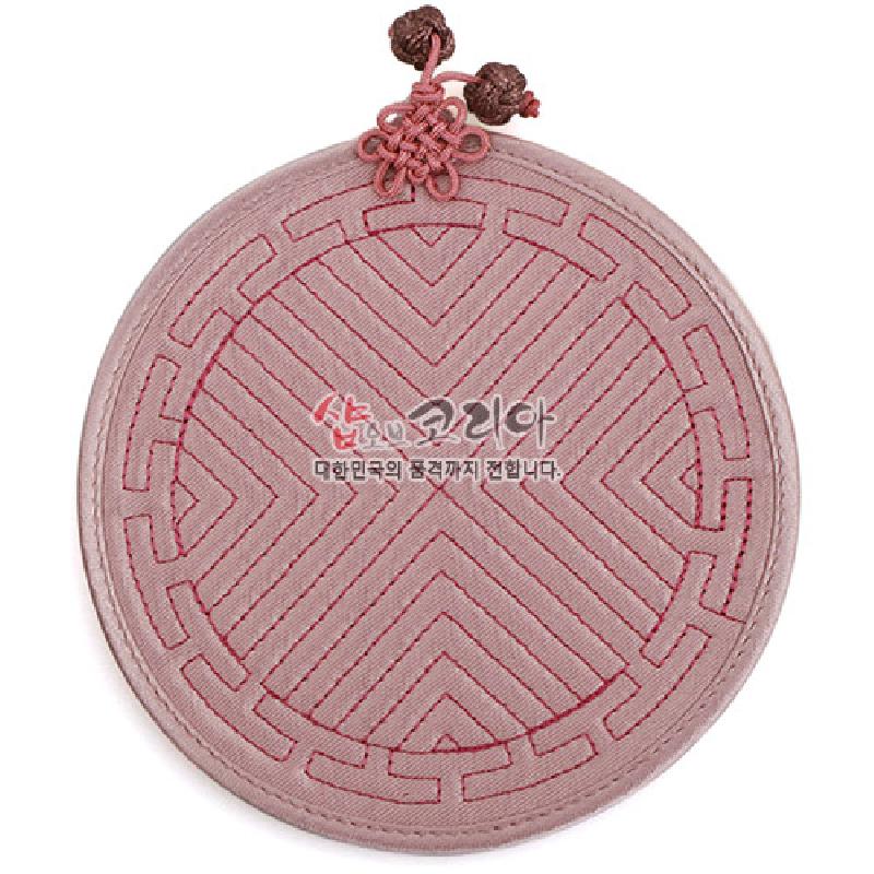 분홍색 천 소재에 전통 누비 기법으로 기하학 문양을 수놓은 원형 컵받침과 매듭 장식.