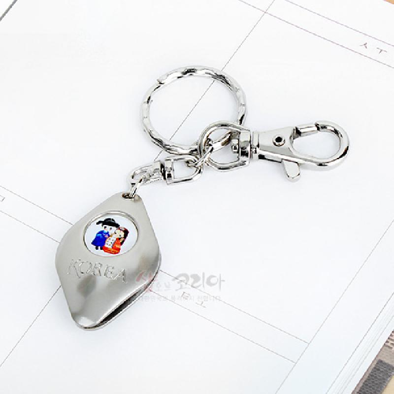 은색 금속 재질에 한복 입은 남녀 일러스트 원형 장식이 더해진 물방울형 열쇠고리. 은색 금속 재질에 한복 입은 남녀 일러스트 원형 장식이 더해진 물방울형 열쇠고리.