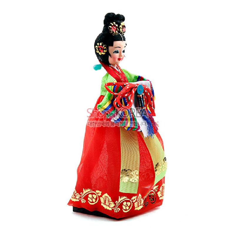 붉은 색 비단 치마와 금색 자수 문양이 어우러진 왕비 한복 인형, 다채로운 노리개와 매듭 장식이 특징인 공예품.