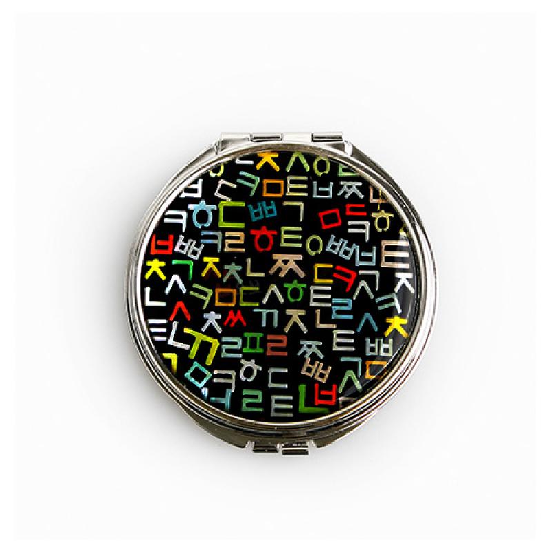 검은 바탕 위에 다채로운 색상의 훈민정음 자음 문양을 인쇄한 금속 테두리 손거울. 검은 바탕 위에 다채로운 색상의 훈민정음 자음 문양을 인쇄한 금속 테두리 손거울.