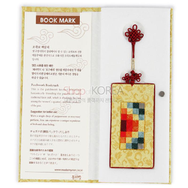 황색 바탕에 전통 조각보 누비 기법과 다색 패치워크 문양이 어우러진 직사각형 책갈피, 붉은 매듭 장식 장식.