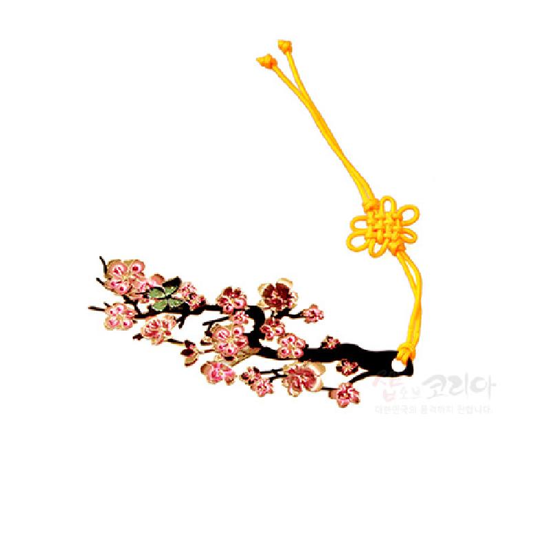 금속 재질 위에 분홍색 매화나무 문양을 넣은 책갈피와 노란색 전통 매듭 끈 장식.