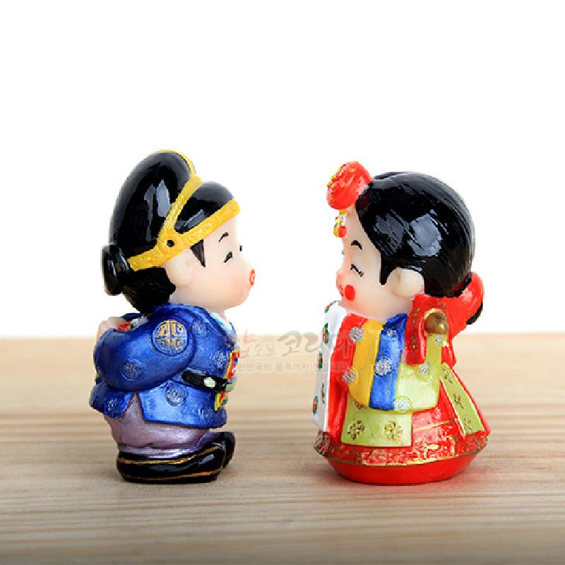 채색 수지 재질의 소형 신랑신부 인형으로, 전통 혼례복의 청·홍·황색 대비와 금색 문양 장식이 특징인 민속 장식품. 채색 수지 재질의 소형 신랑신부 인형으로, 전통 혼례복의 청·홍·황색 대비와 금색 문양 장식이 특징인 민속 장식품.